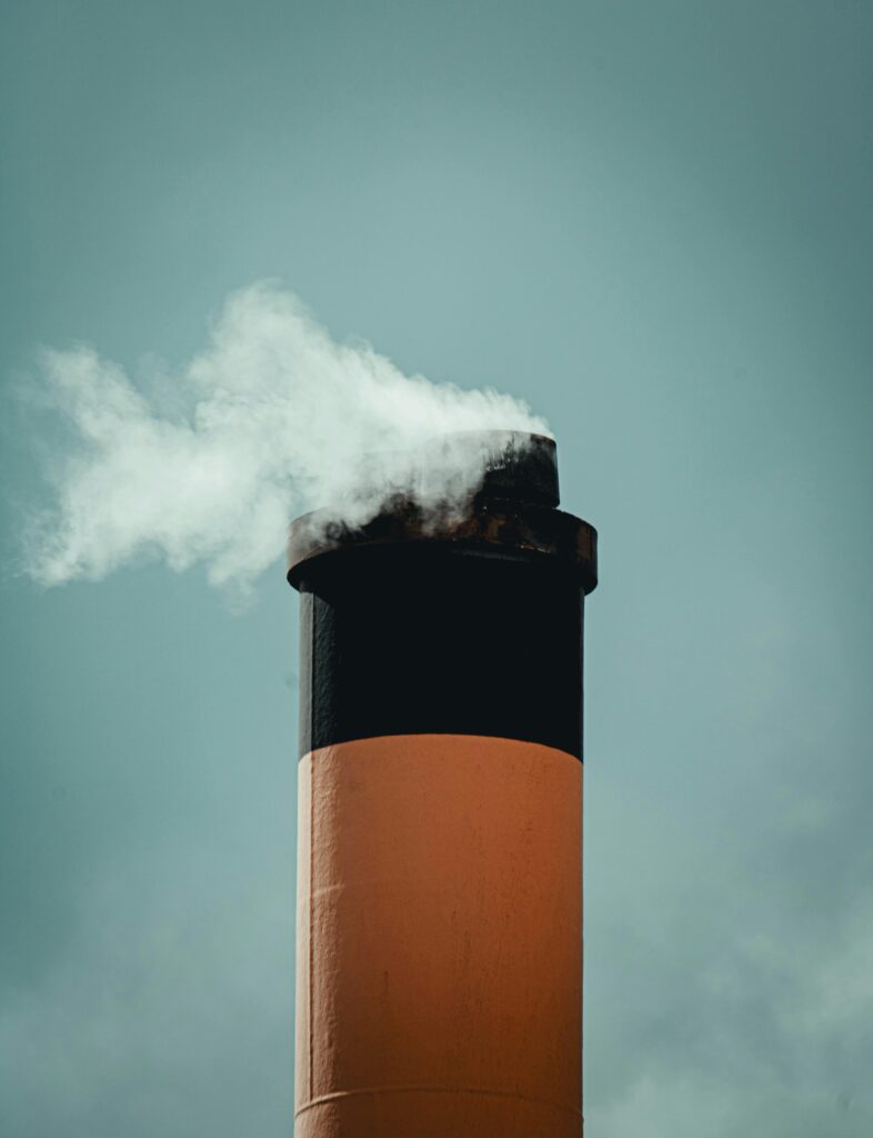 A tall industrial chimney emits smoke into the sky, symbolizing air pollution.